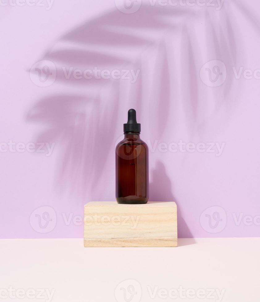 A brown glass bottle with a pipette on purple background. photo