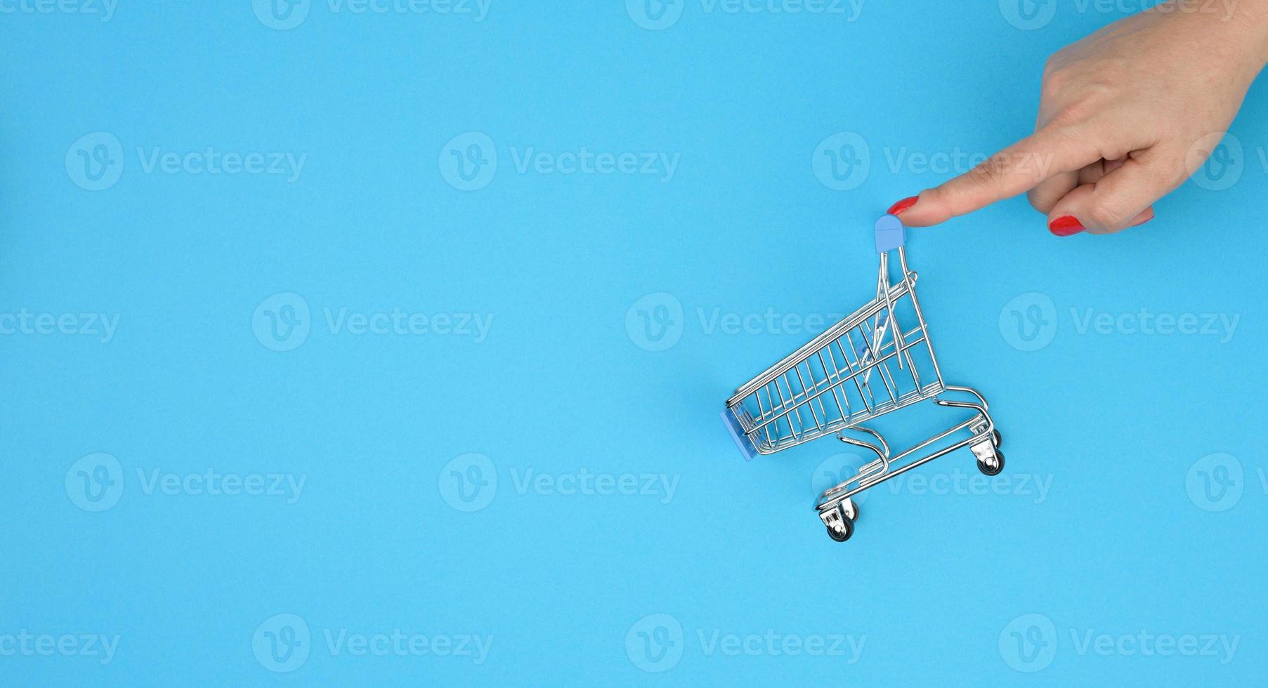 female hands hold an empty metal miniature trolley on a blue background. Sale concept photo