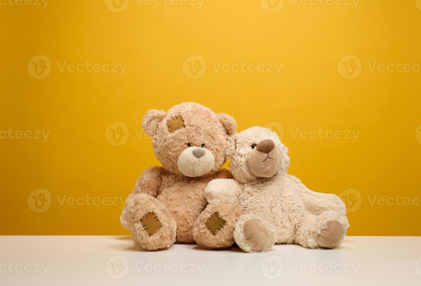 two cute brown teddy bears sitting on a yellow background, childrens toy photo