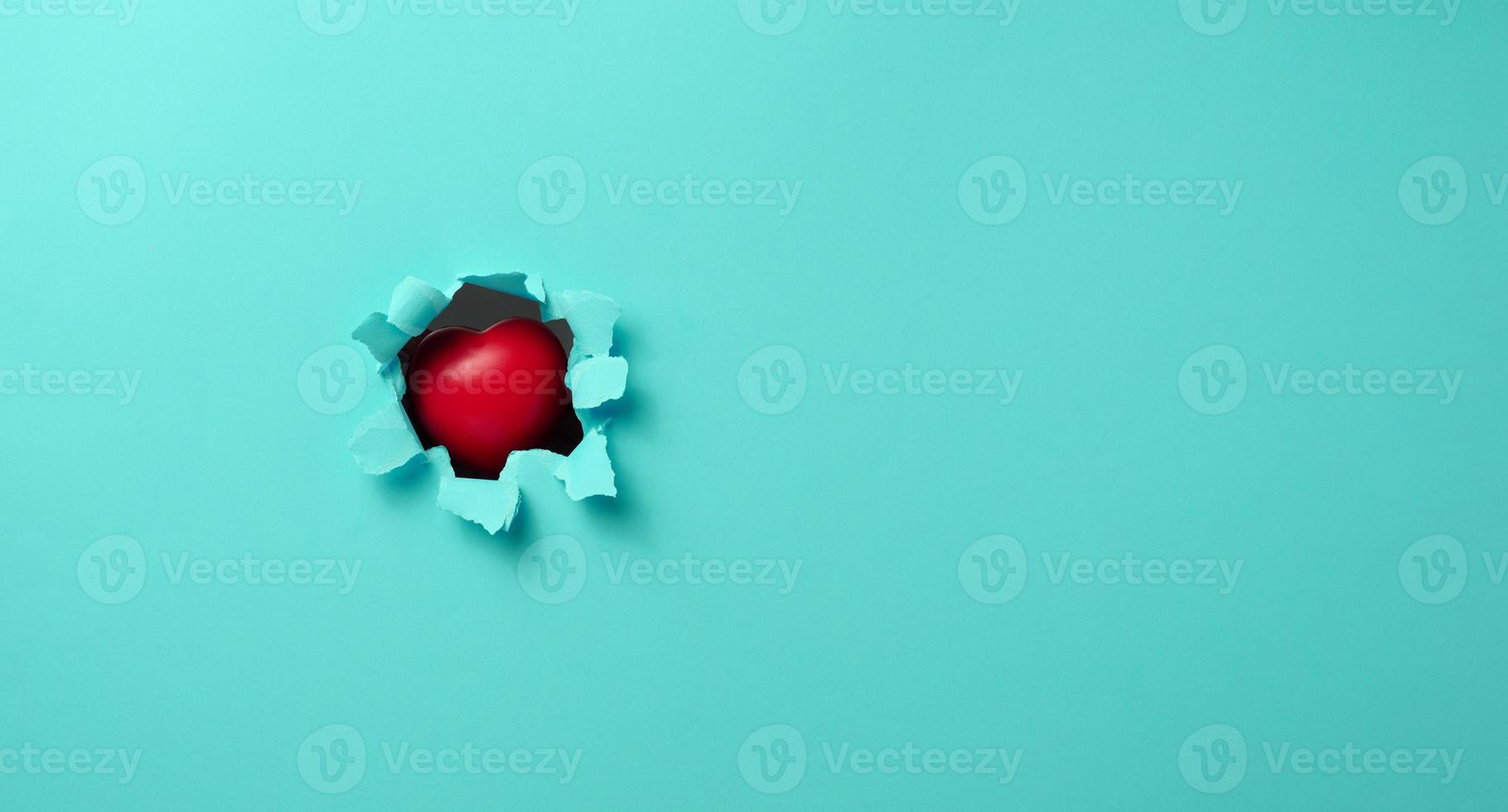 red heart sticks out in a hole with torn edges in blue paper photo