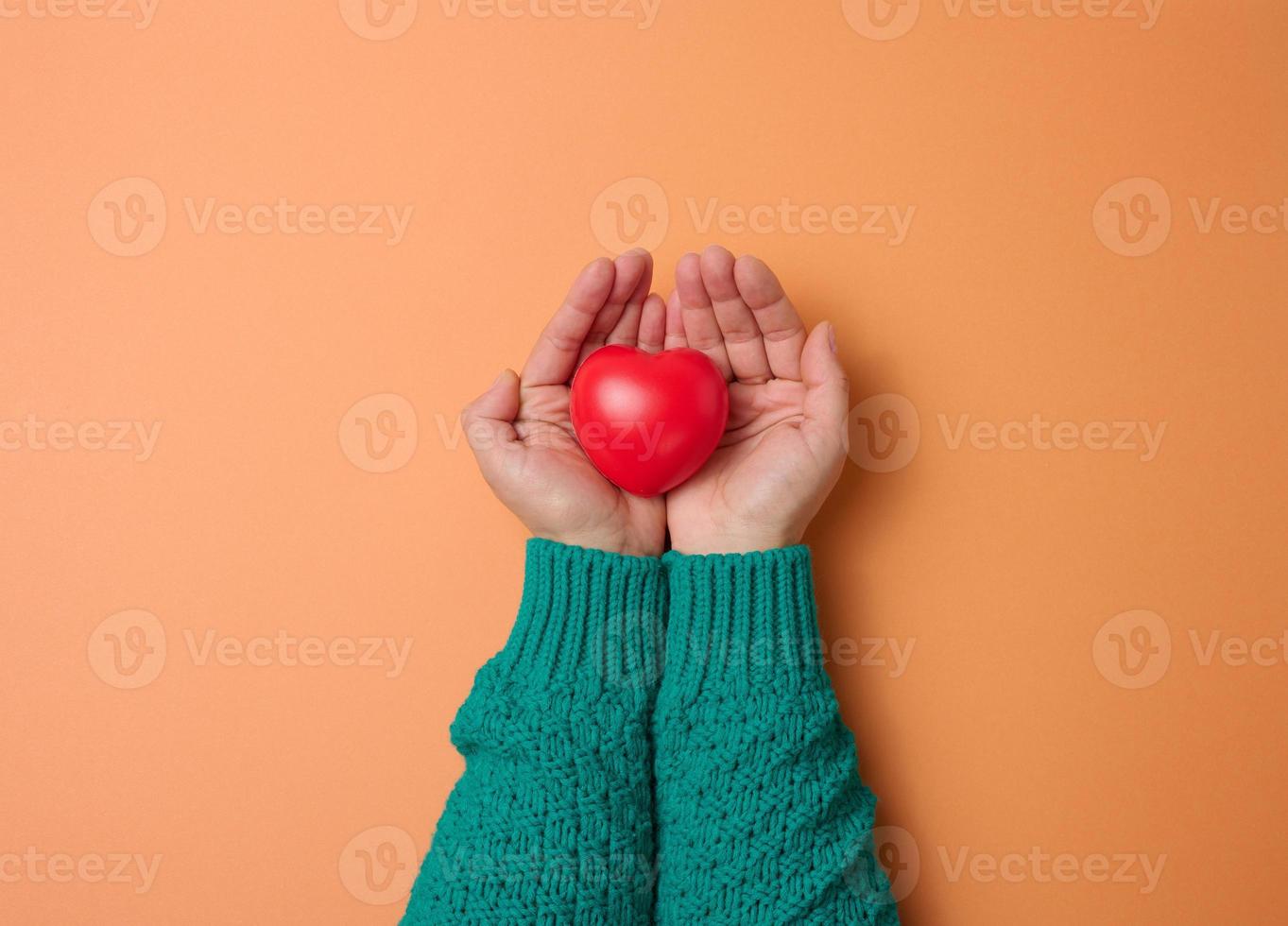 female hands holds red heart, orange background. Love and donation concept photo