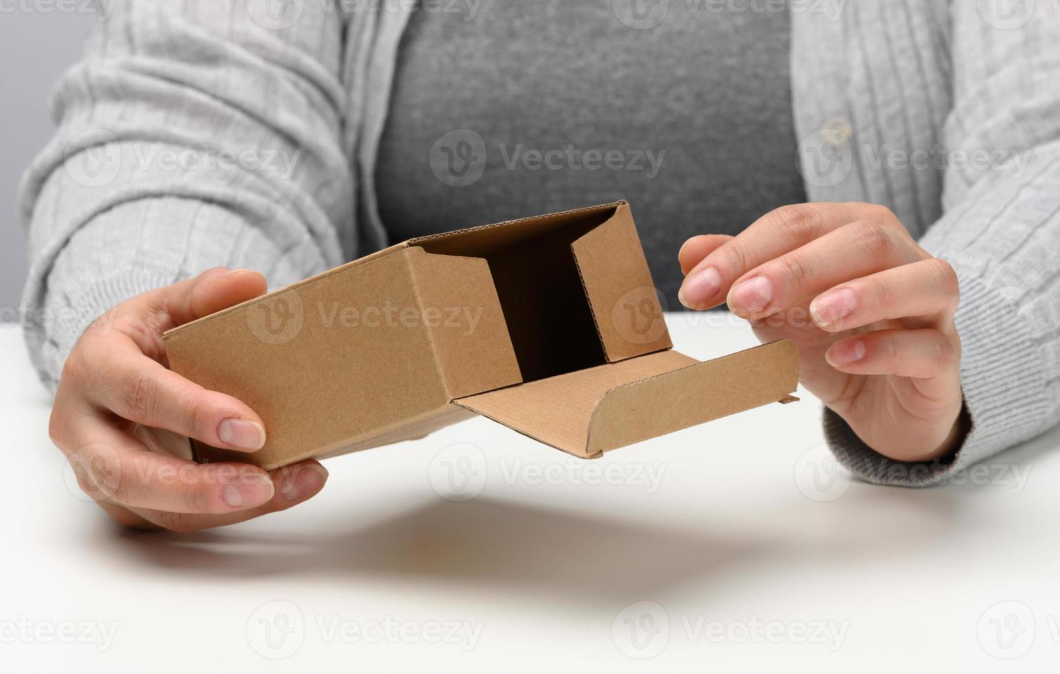 two female hands hold a square box made of brown corrugated cardboard on a white background, close up photo