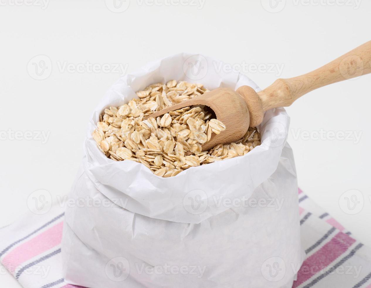 raw oatmeal in a white paper bag and a wooden spoon on a white table, breakfast porridge photo