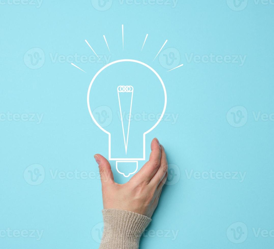 Woman's hand and a drawn electric lamp on a blue background. The concept of searching for ideas and solutions, brainstorming. Switching to alternative forms of energy photo