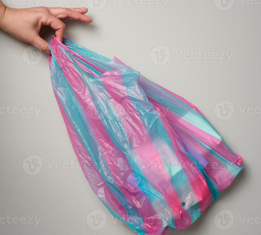 female hand holds full plastic bag on gray background, top view photo