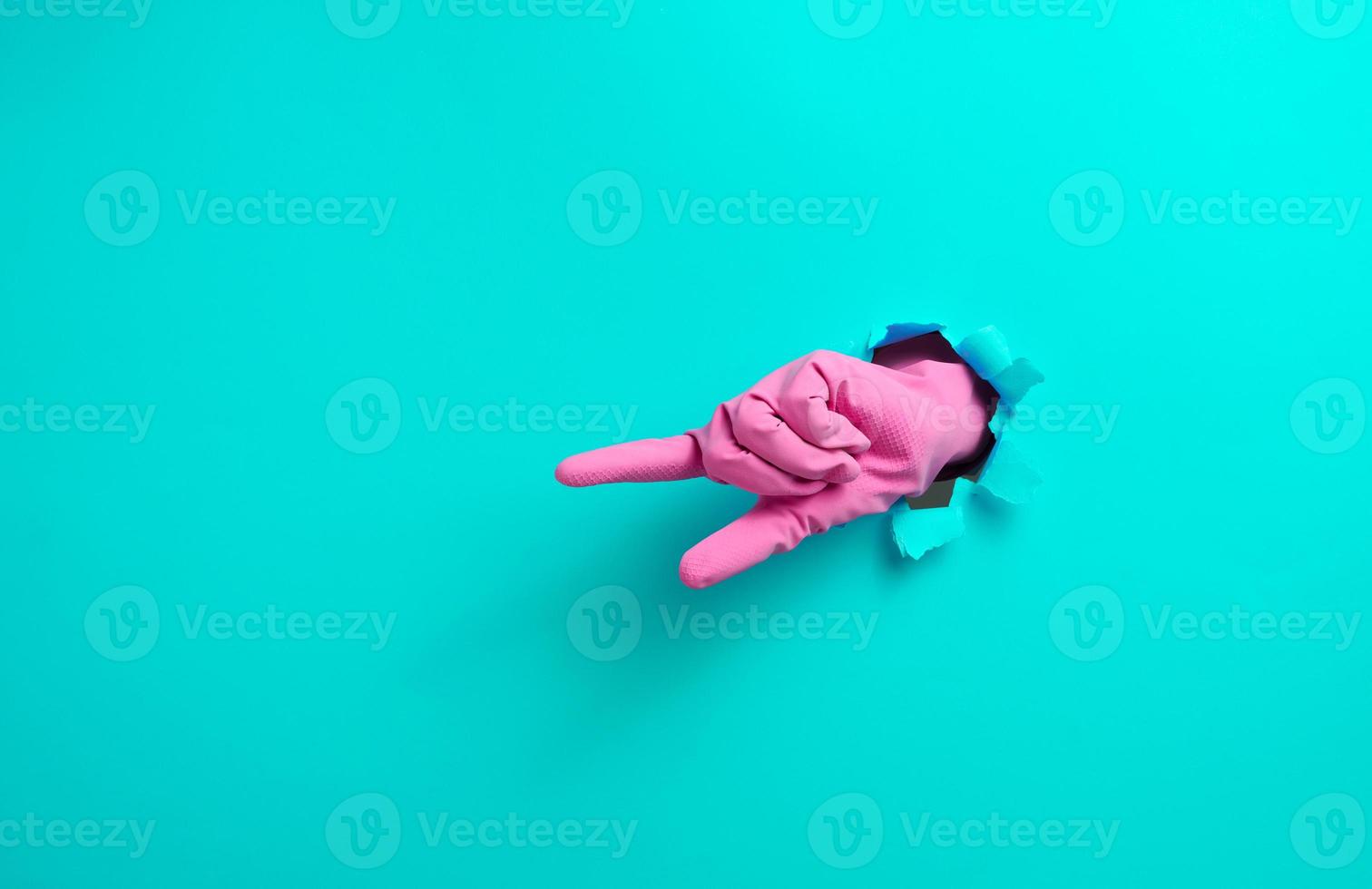 hand in a pink latex glove points a finger on a blue background. Place for inscription of discounts, offer or announcement. photo