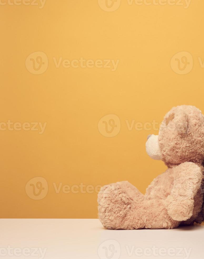 brown cute teddy bear sits sideways on yellow background, sadness photo
