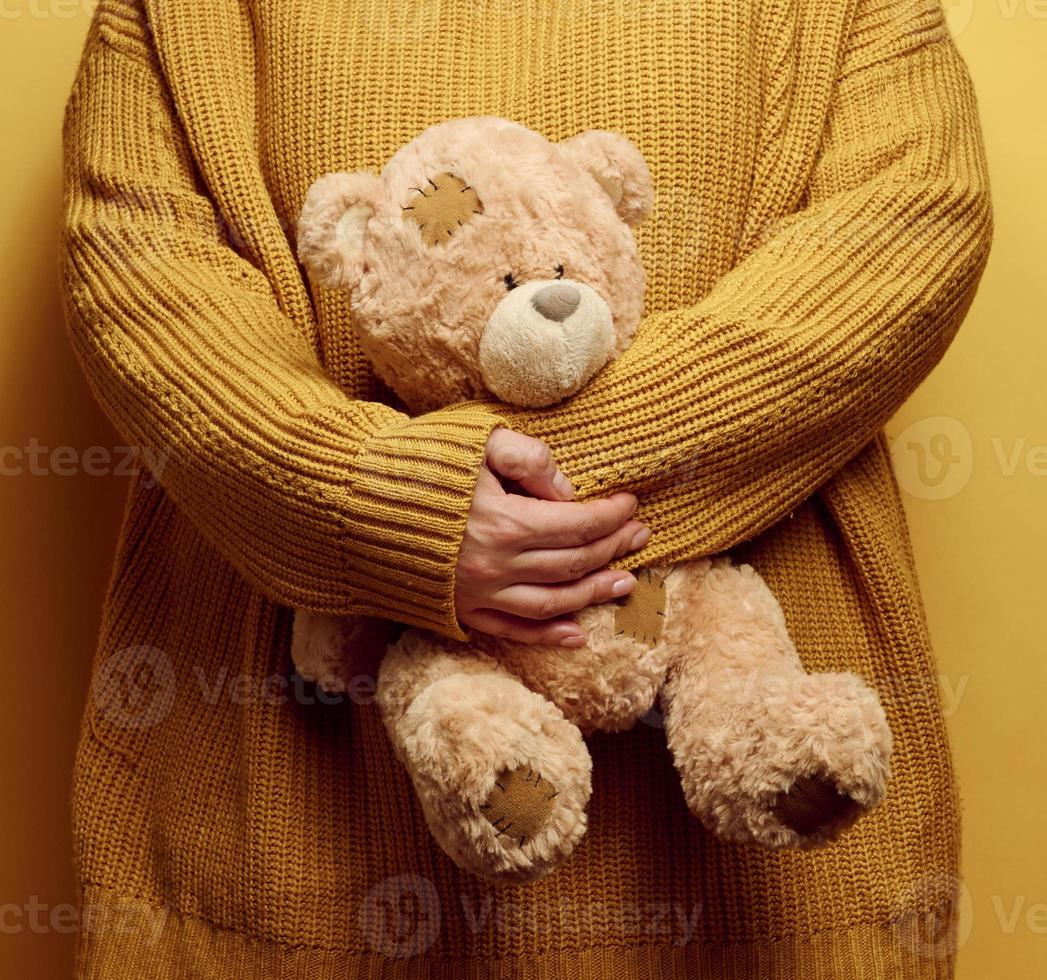 woman in orange knitted sweater hugs cute brown teddy bear. The concept of loneliness and sadness, depression photo