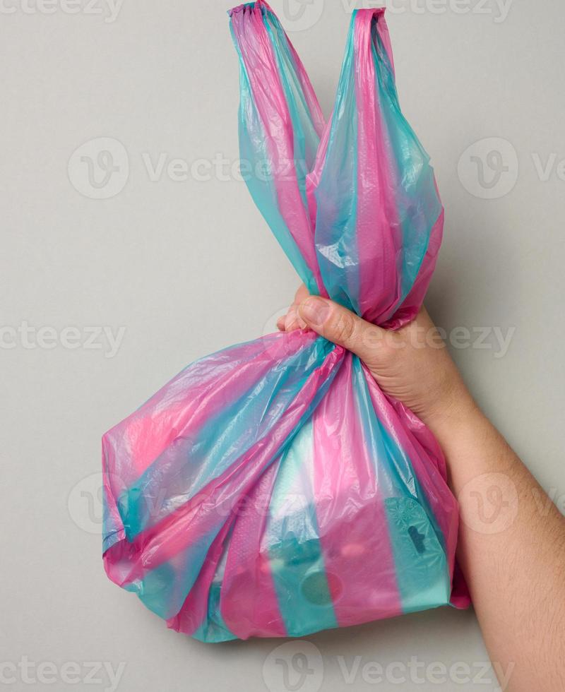 female hand holds full plastic bag on gray background, top view photo