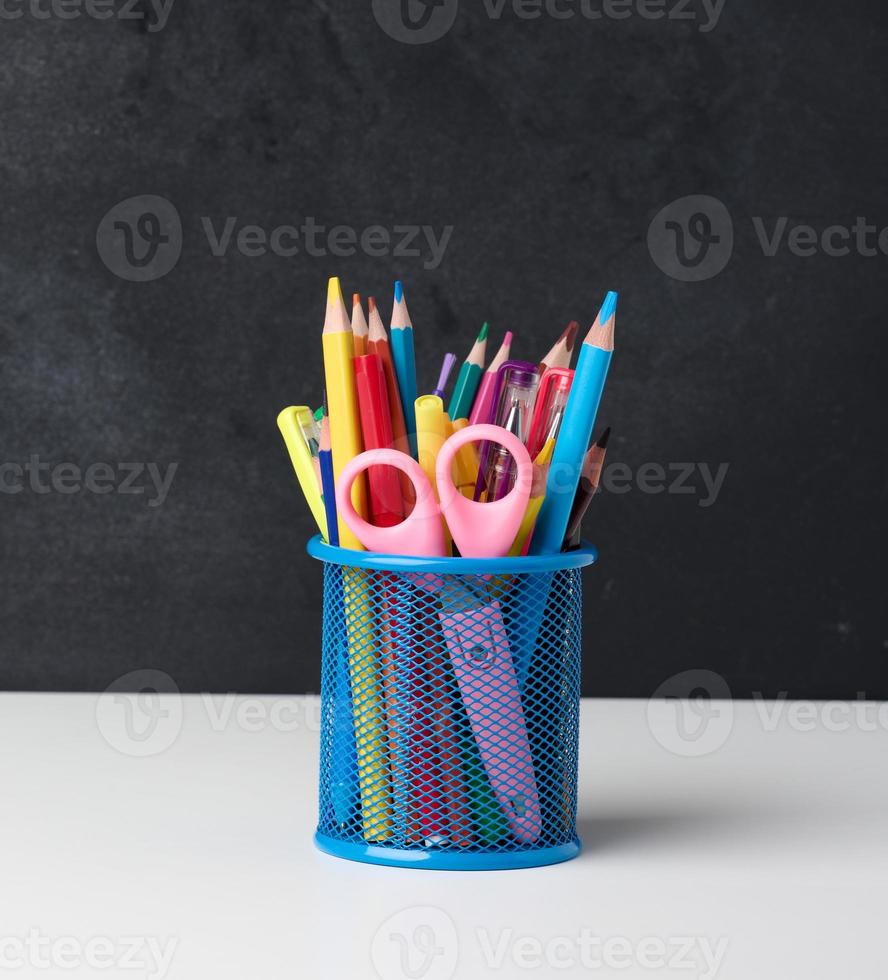 metal glass with pens, pencils and felt-tip pens and scissors on the background of an empty black chalk board photo