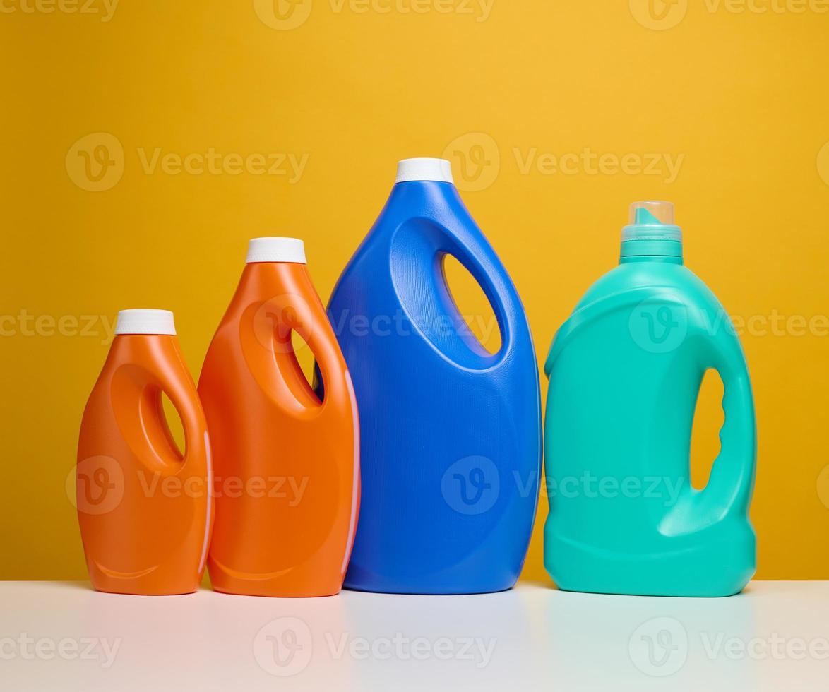 plastic orange and blue large bottles with liquid detergent stand on a white table, yellow background photo