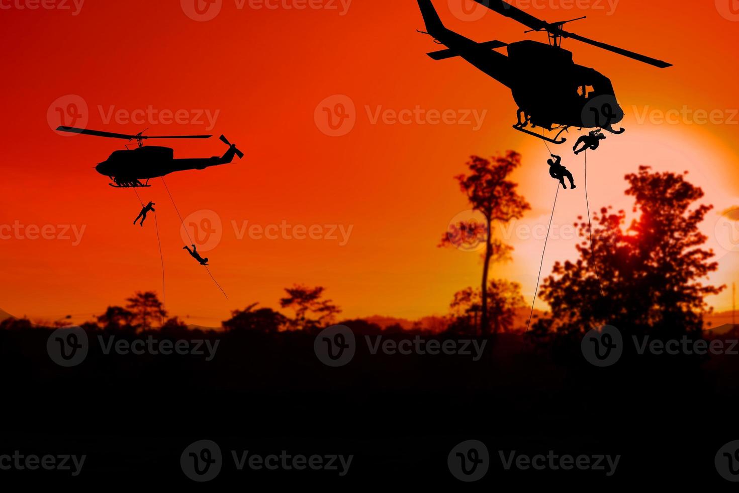 Silhouette Soldiers rappel down to attack from helicopter with sunset and copy space add text photo