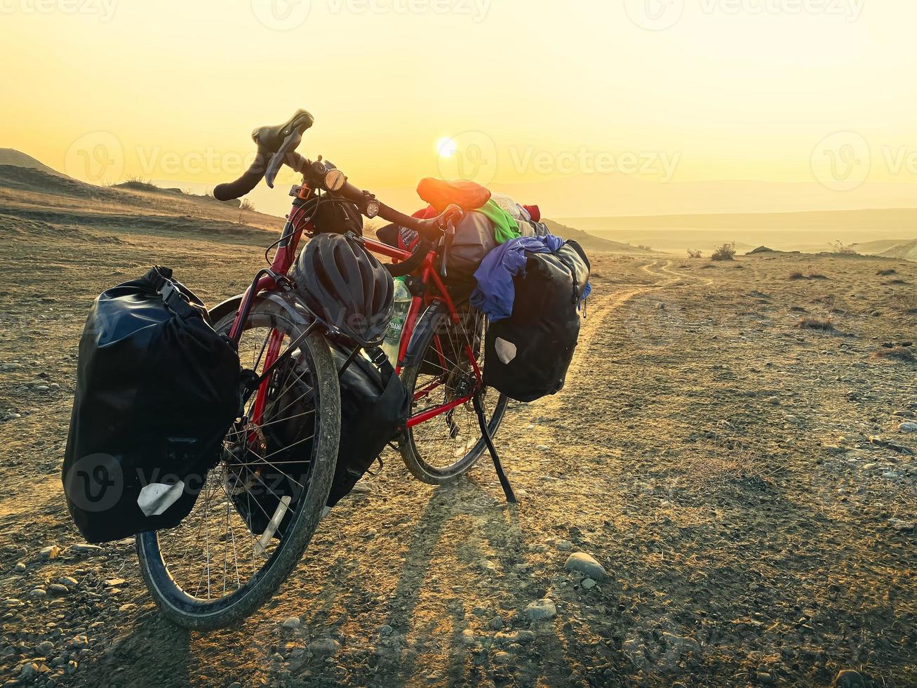 Loaded with bags red bicycle stands on side of road surrounded by mountains in countryside of VAshlovani national park. Bicycle touring holiday in Georgia photo