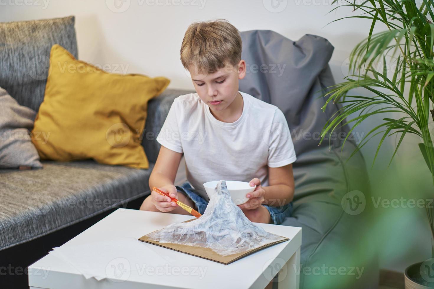 Schoolboy makes creative project in form of papier mache mountain. photo