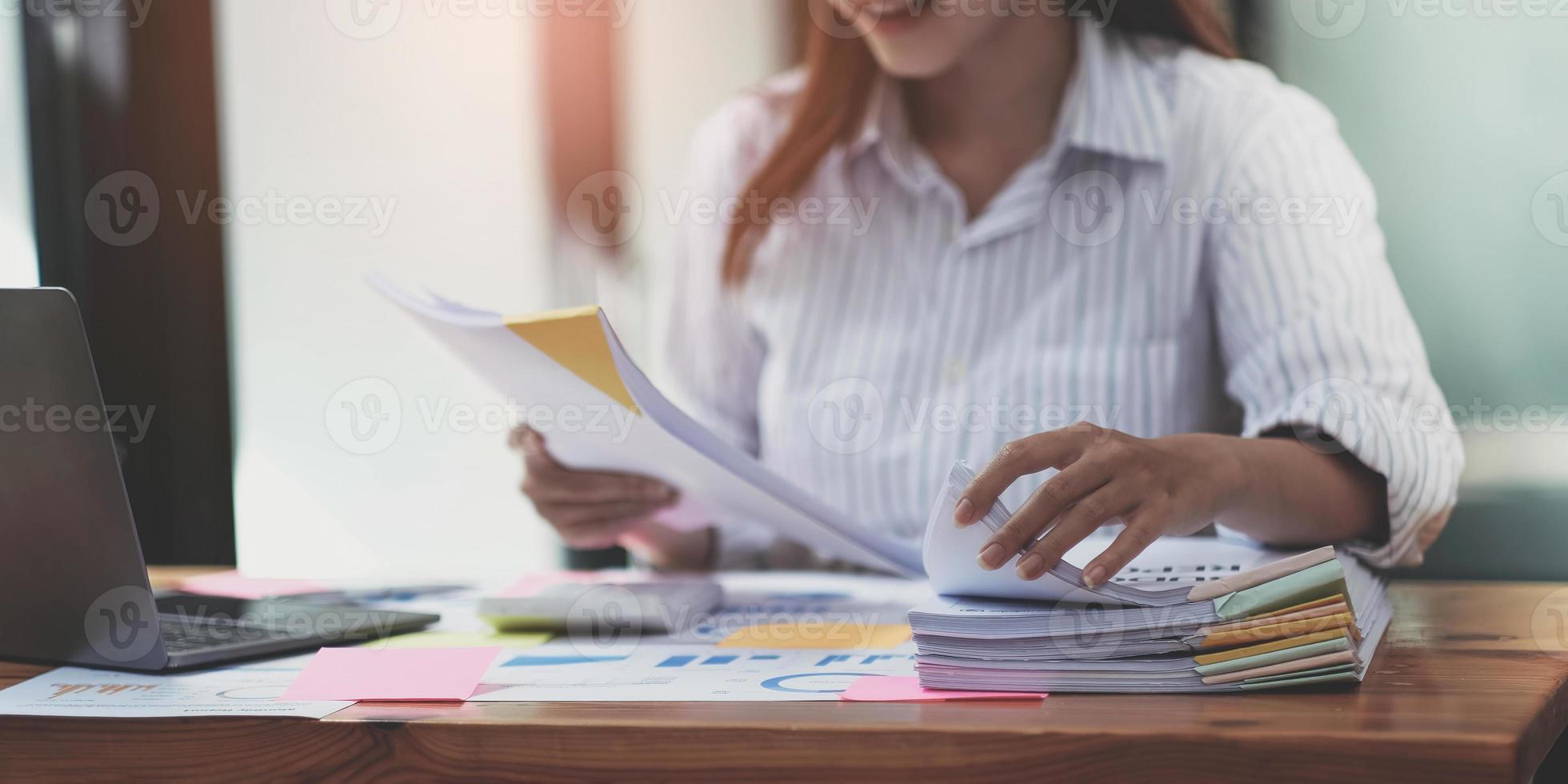 Business Documents concept  Employee woman hands working in Stacks paper files for searching and checking unfinished document achieves on folders papers at busy work desk office. Soft focus photo