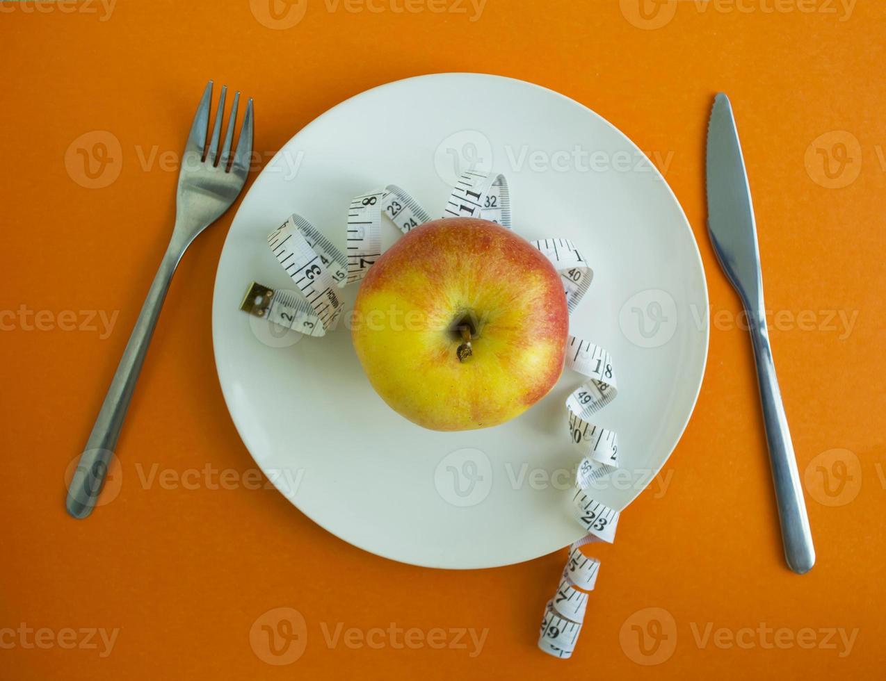 An apple and a centimeter tape in a plate, a fork and a knife photo