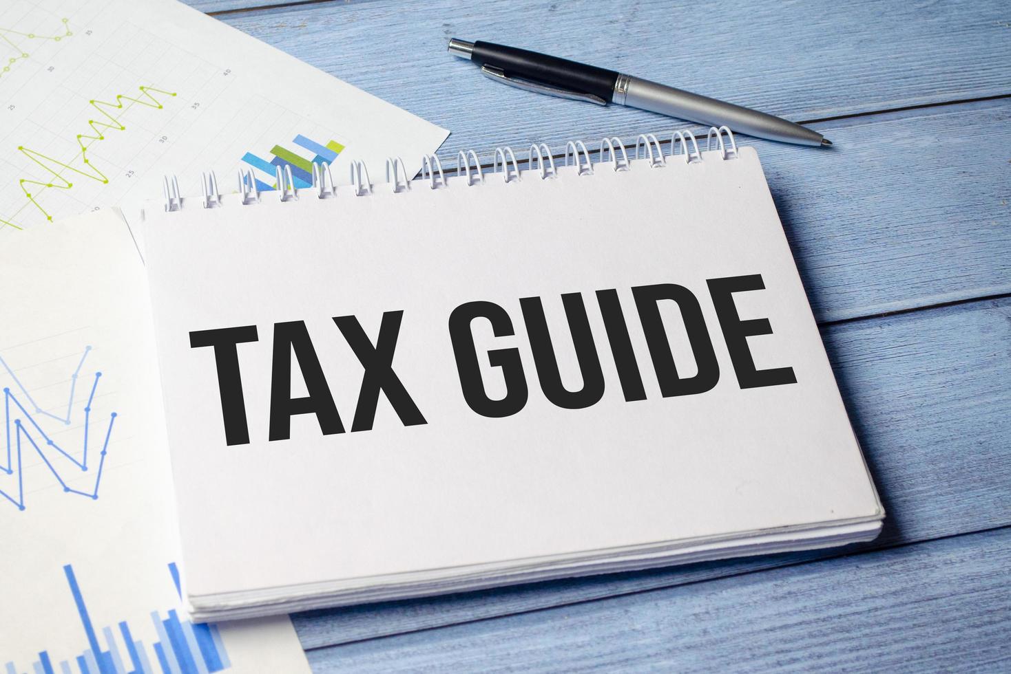 A notepad with the text TAX GUIDE, a pen, calculator and glasses photo