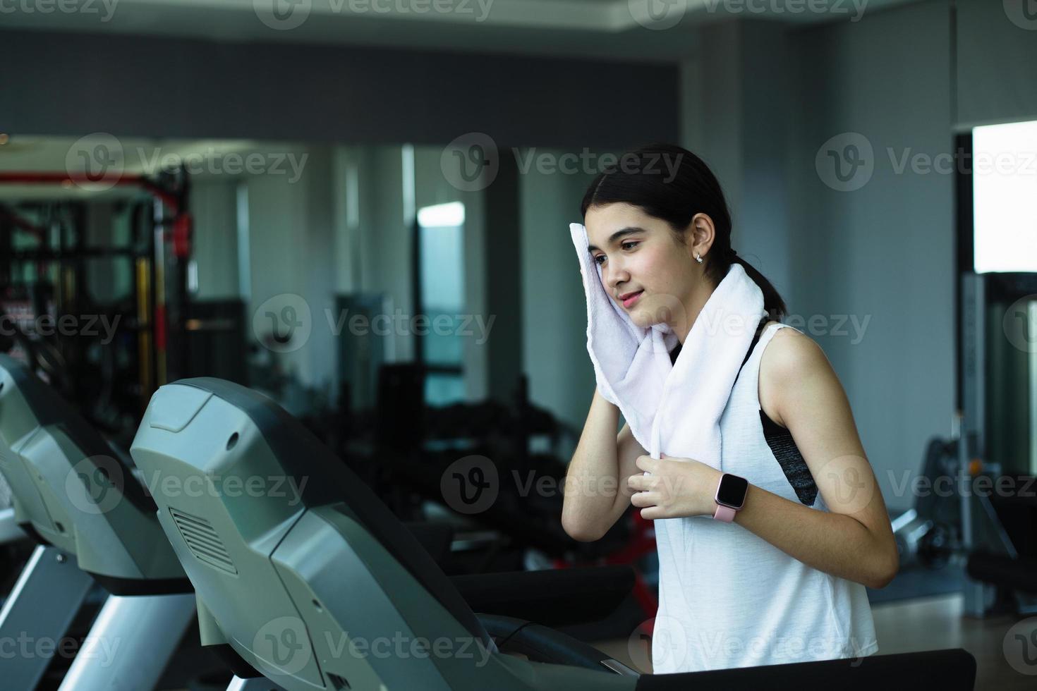 Side view of beautiful girl running on treadmill at gym photo