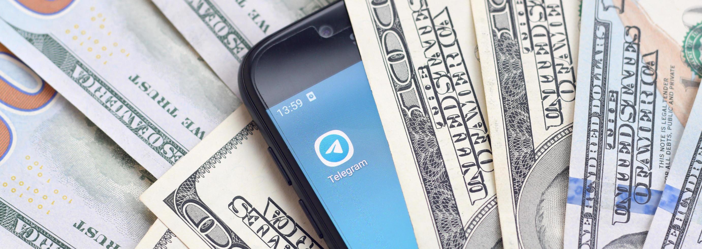 KHARKOV, UKRAINE - MAY 3, 2022 Smartphone screen with Telegram app and lot of hundred dollar bills. Business and social networking concept photo