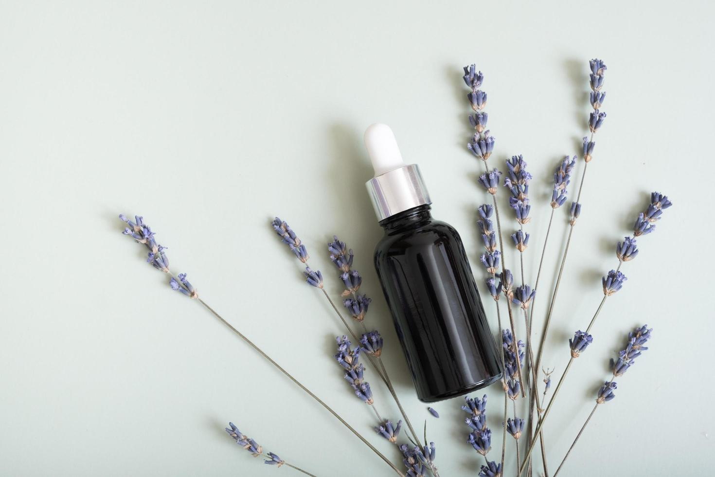 Cosmetic bottle with pipette on wooden slice  top view, flat lay on colored background with lavender flowers. Natural cosmetic concept photo