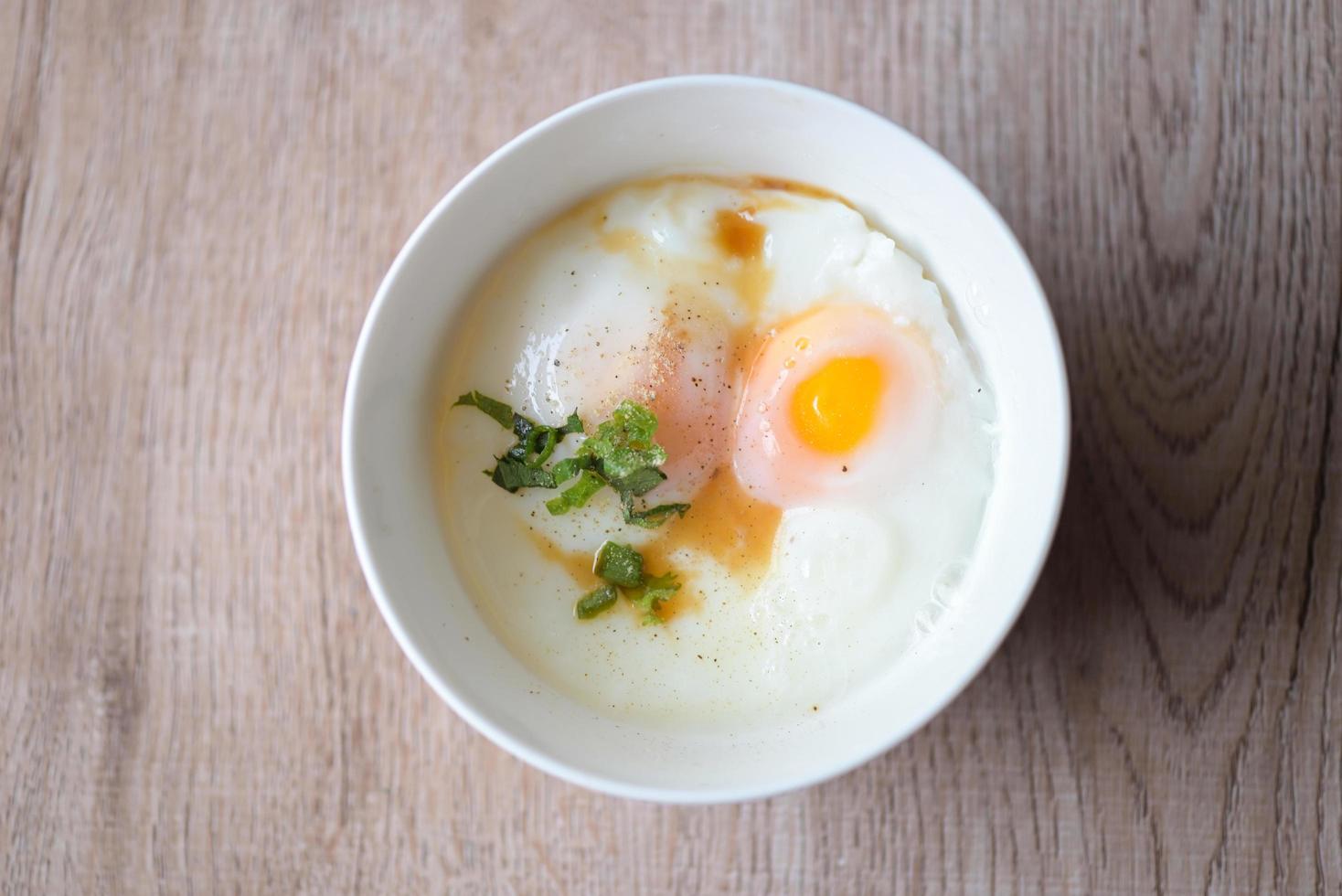 desayuno de huevo, huevos pasados por agua en un tazón blanco con pimienta, cilantro en una mesa de madera, huevo onsen tamago - microondas de huevo foto