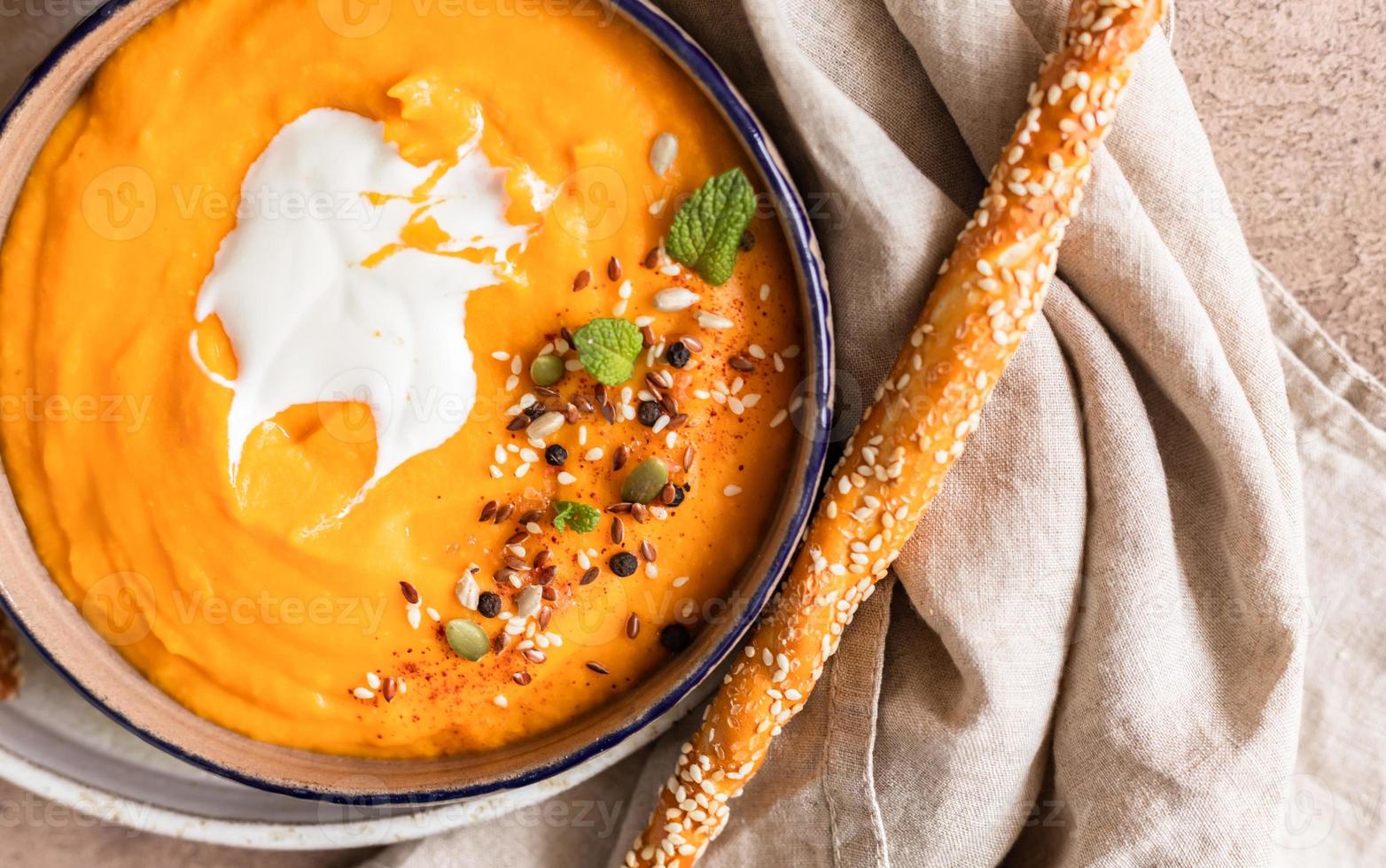 Pumpkin and carrot soup with cream, mint and seeds, brown concrete background. Traditional autumn or winter vegetarian soup with a creamy silky texture. photo
