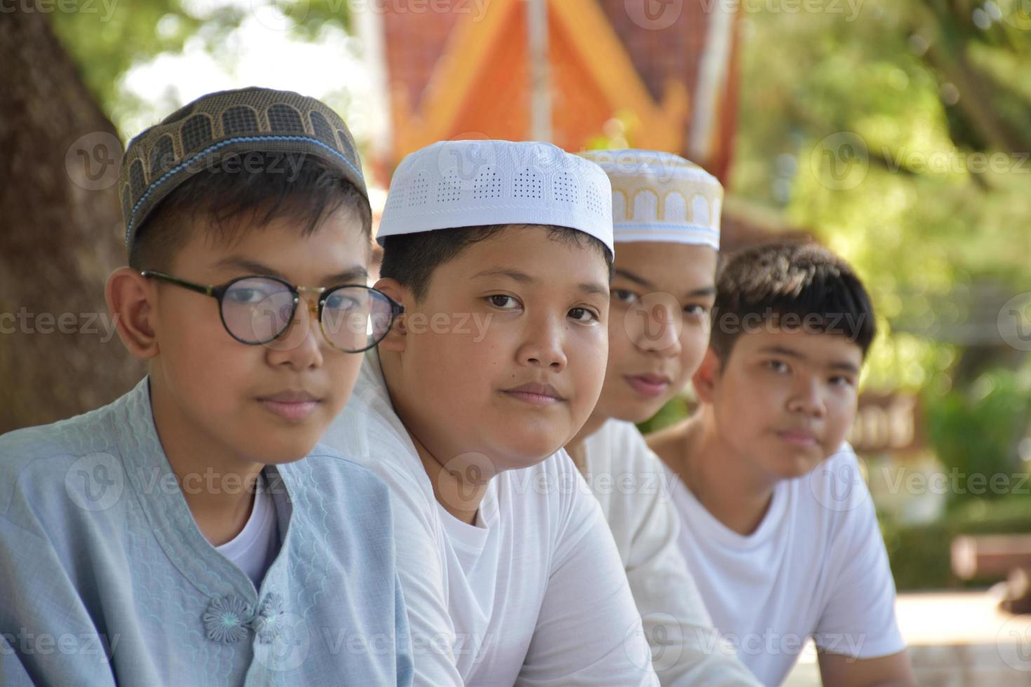 Young asian muslim boys sit in a row under the tree in the school park during their free times, soft and selective focus. photo