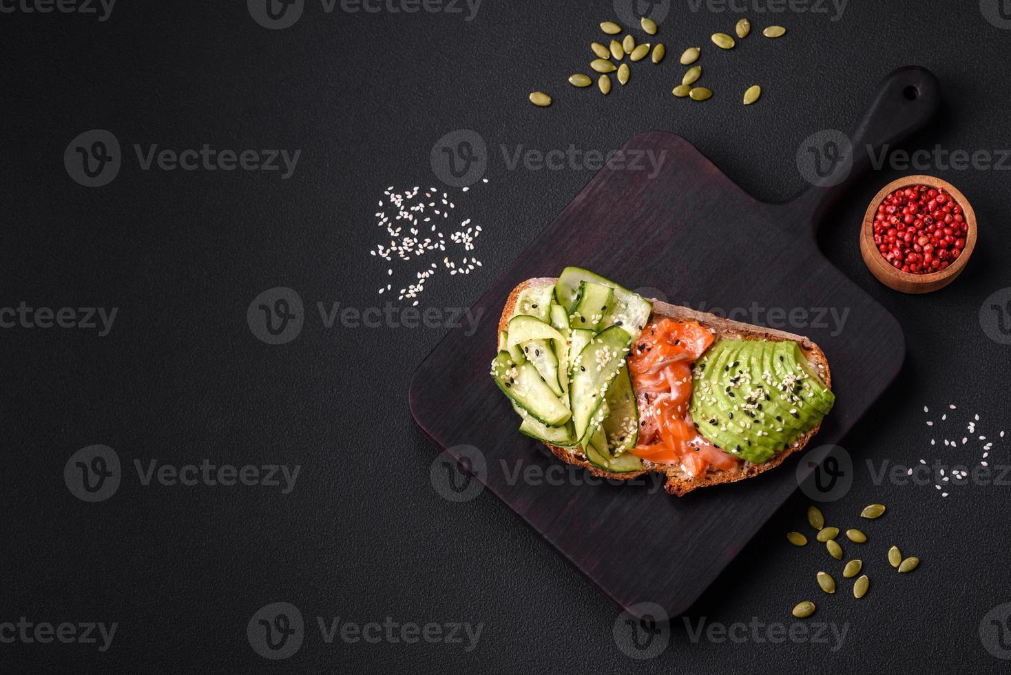 Delicious brown bread toast with salmon, avocado, cucumber and sesame seeds photo