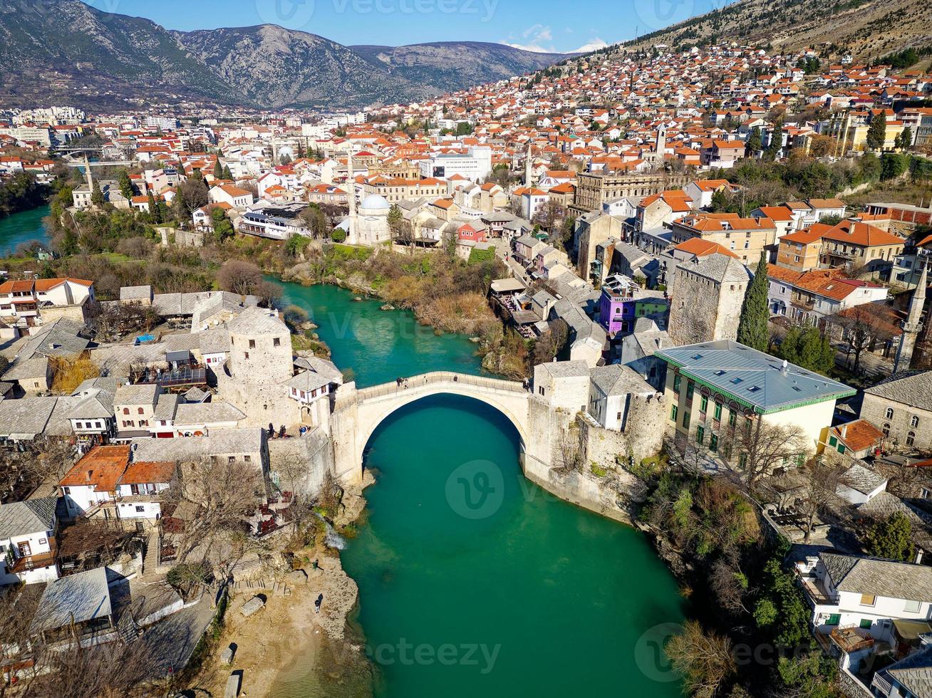 Aerial drone view of the Old Bridge in Mostar city in Bosnia and Herzegovina during sunny day. Blue turquoise colors of Neretva river. Unesco World Heritage Site. People walking over the bridge. photo