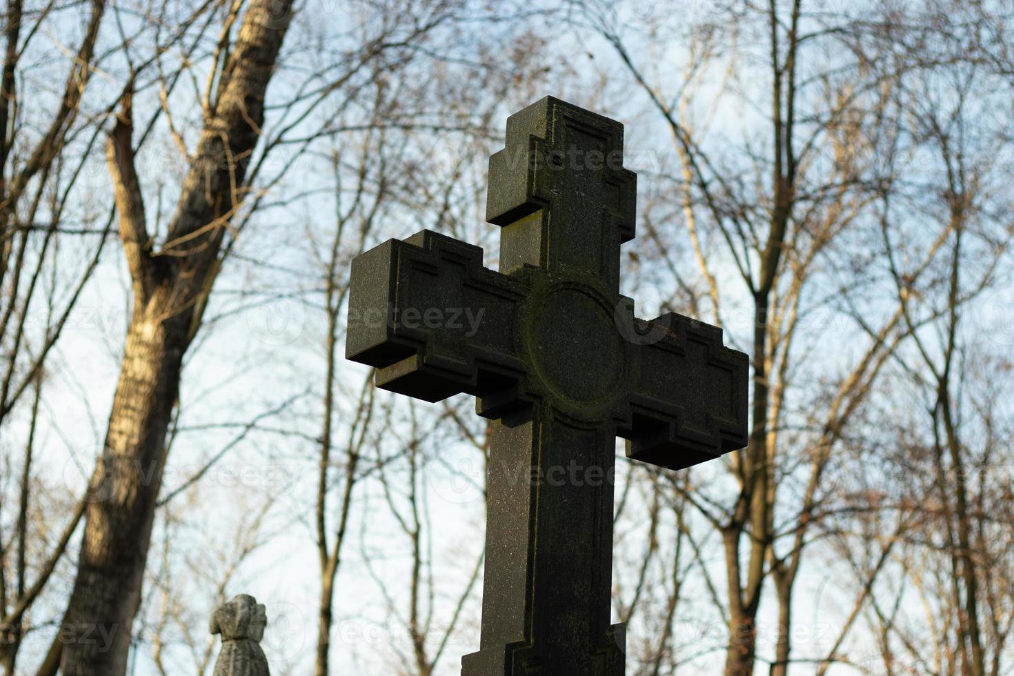 Large Christian cross made of dark stone against the background of tree branches and sky. Religion concept photo