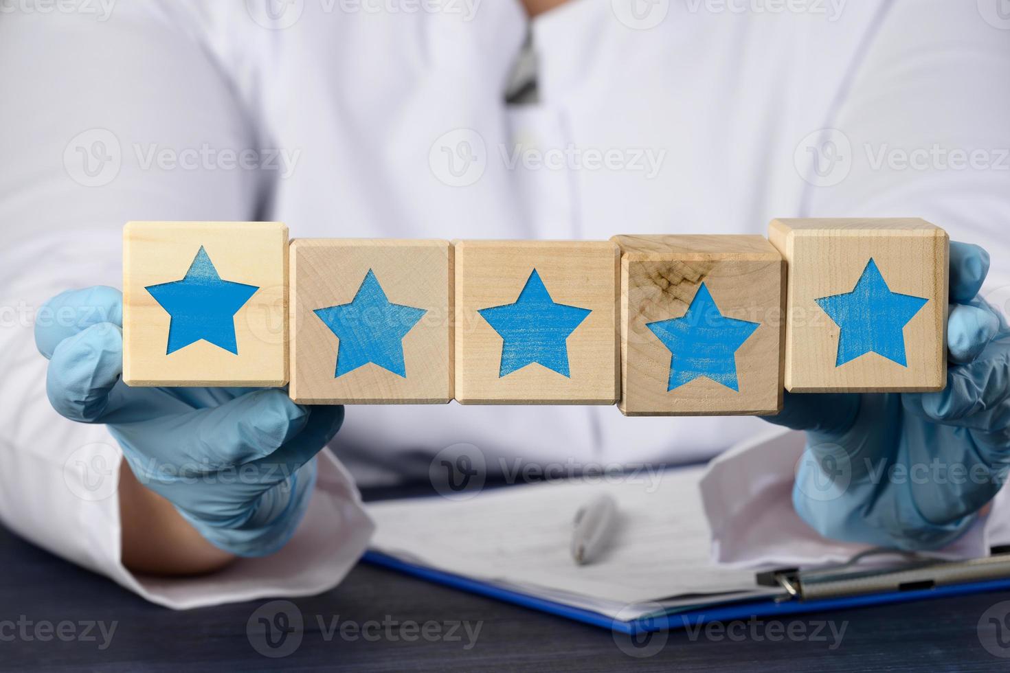 médico en azul guantes sostiene cubitos con cinco estrellas. Servicio calidad evaluación y clasificación concepto foto