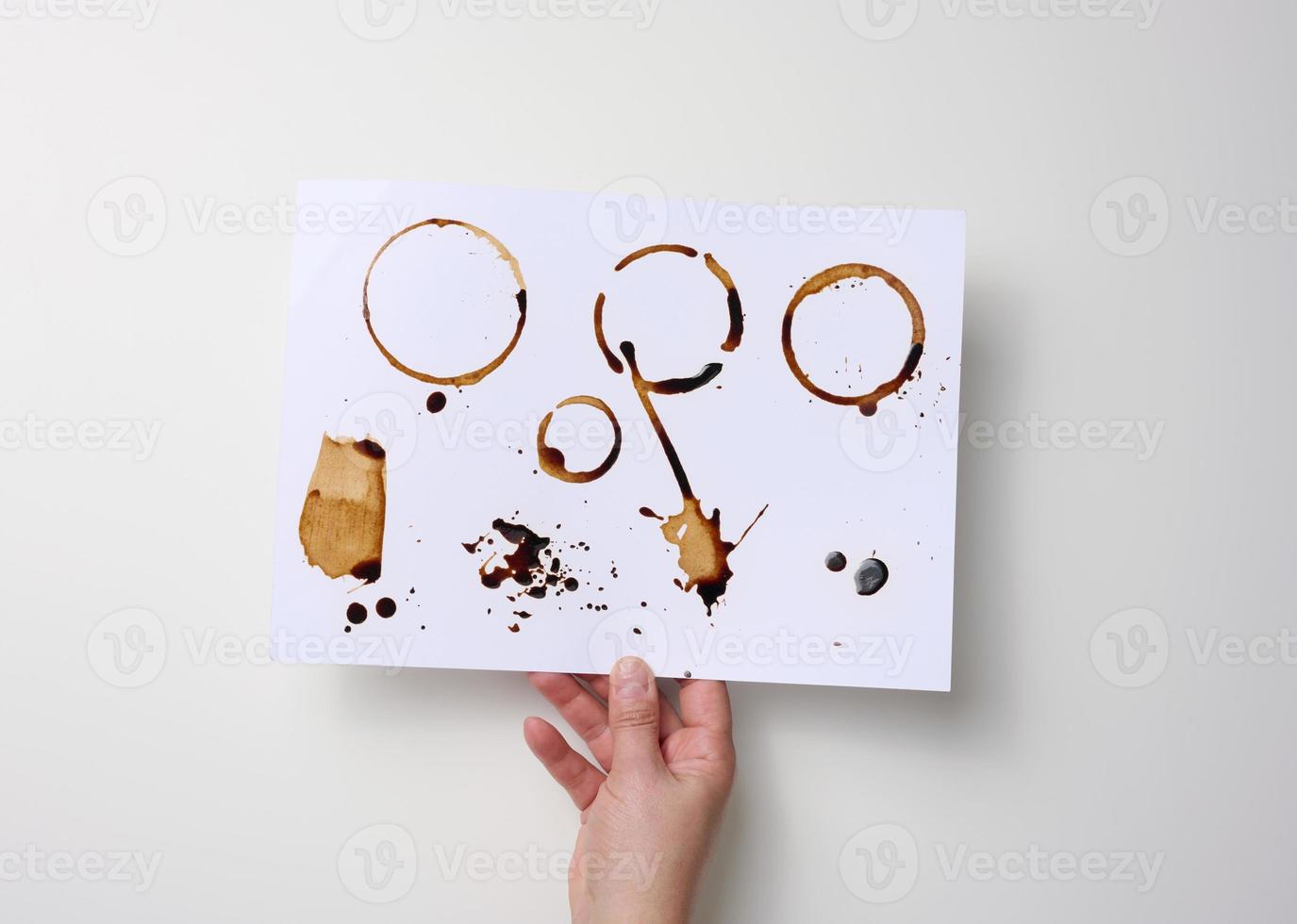 female hand holds a white sheet of paper with brown prints from the bottom of a cup with coffee photo