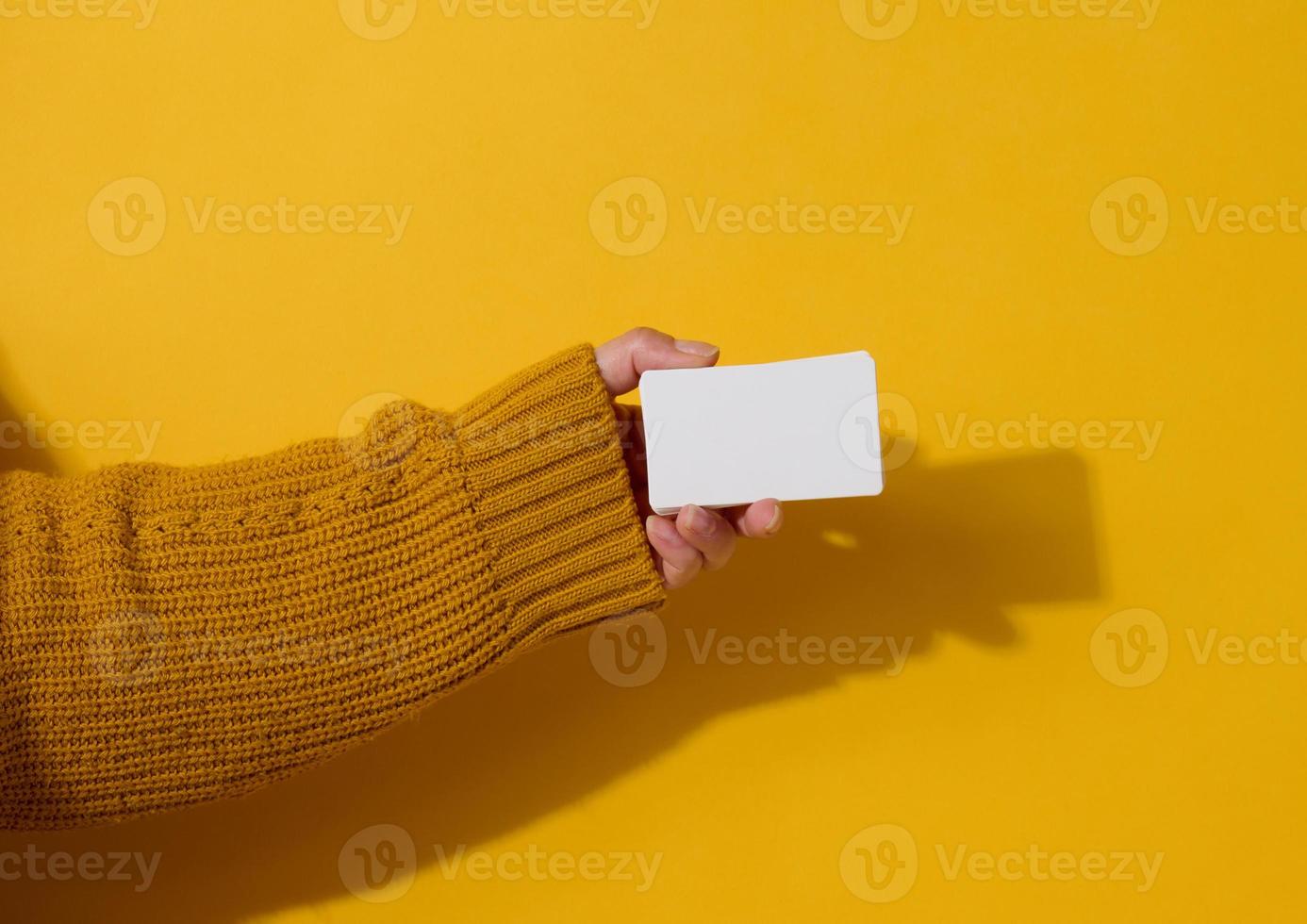 Female hand holding empty paper white business card on a yellow background. Copy space photo