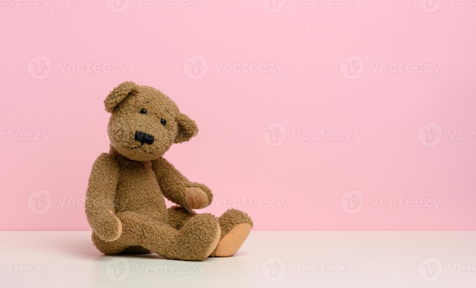 marrón osito de peluche oso con parches se sienta en un blanco mesa, rosado antecedentes foto