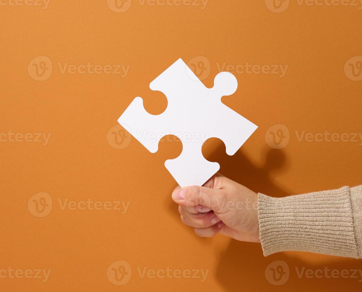 female hand holds a fragment of a white large puzzle on a brown background, the concept of finding an idea, solving a problem photo