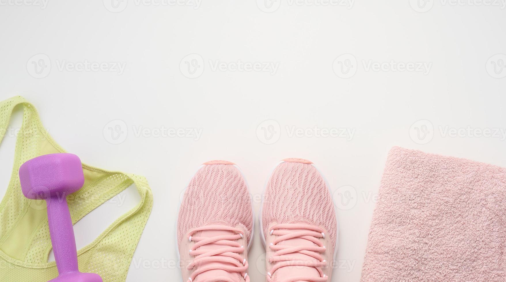 a pair of pink sneakers, a terry towel and a plastic dumbbell on a white background, top view photo