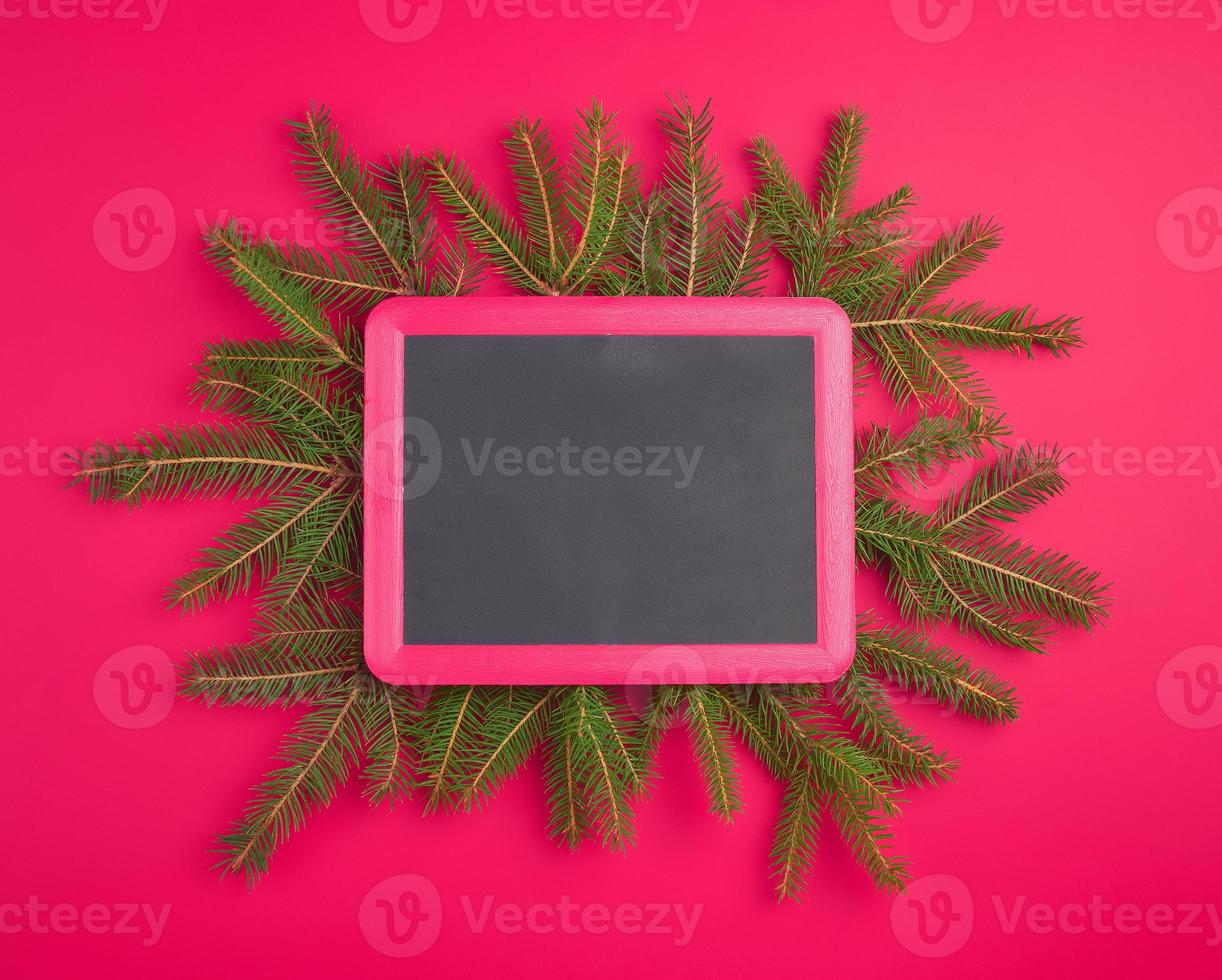 empty black chalk frame, green branches of spruce on a red background photo