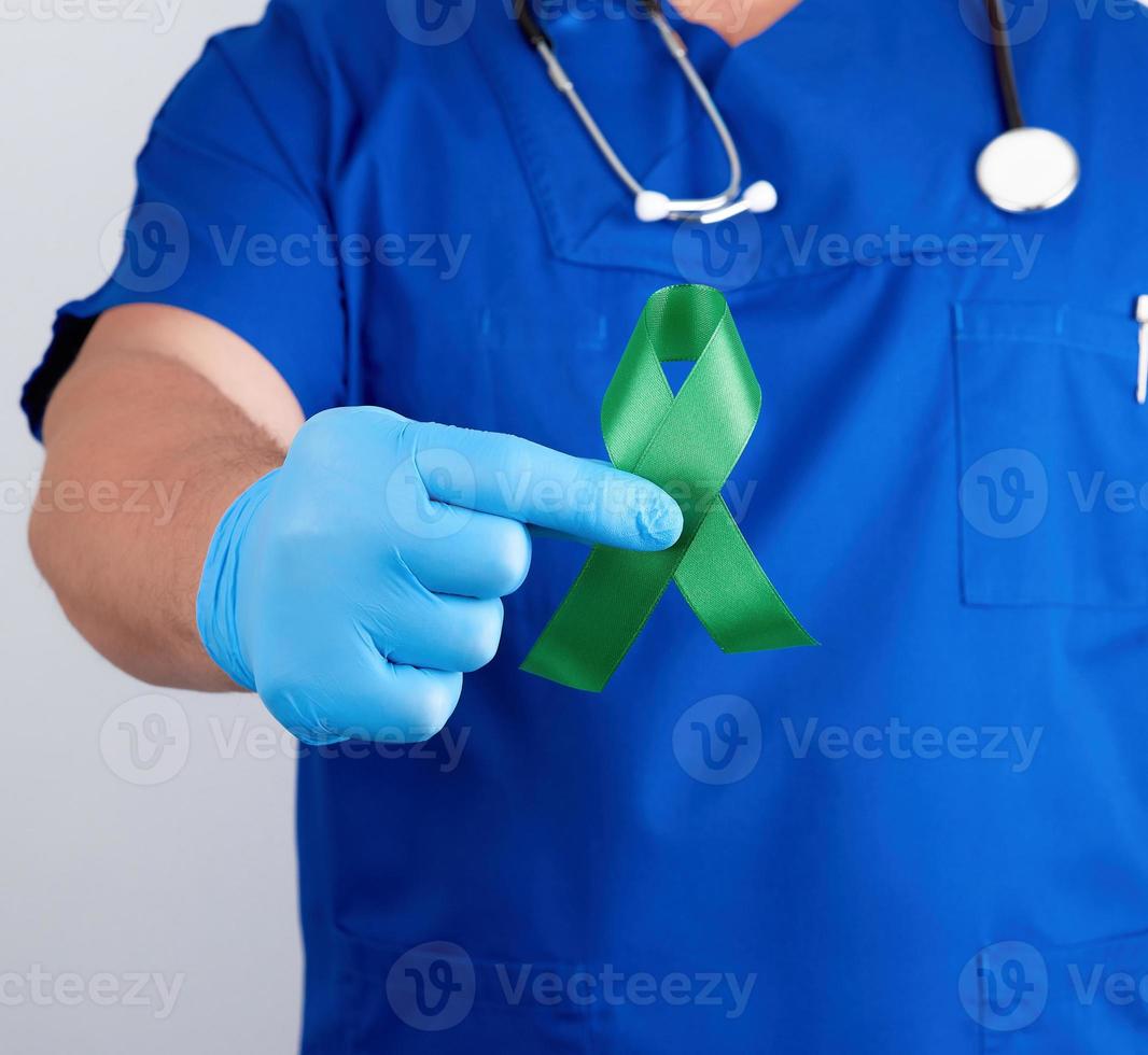 doctor in blue uniform and latex gloves holds a green ribbon photo