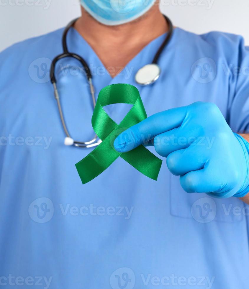 doctor in blue uniform and latex gloves holds a green ribbon photo