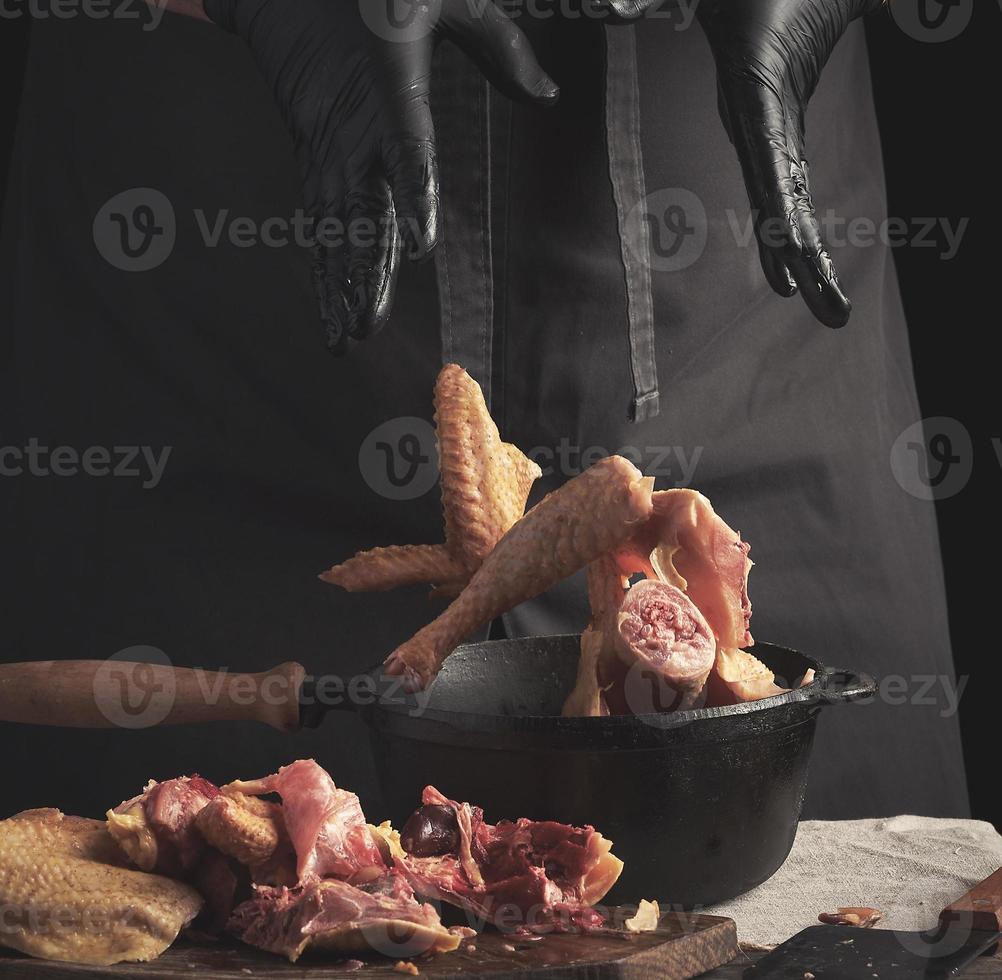 chef in black uniform and latex gloves chopping throws sliced chicken into a black cast-iron frying pan with a wooden handle photo