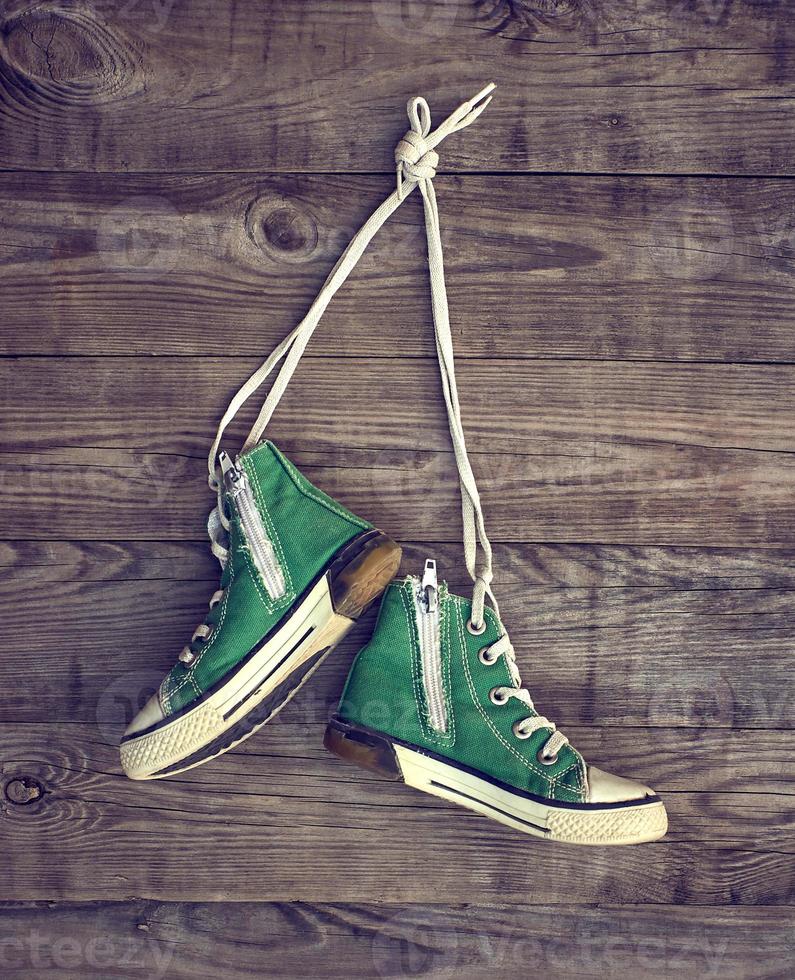 pair of old green textile sneakers hang from laces photo