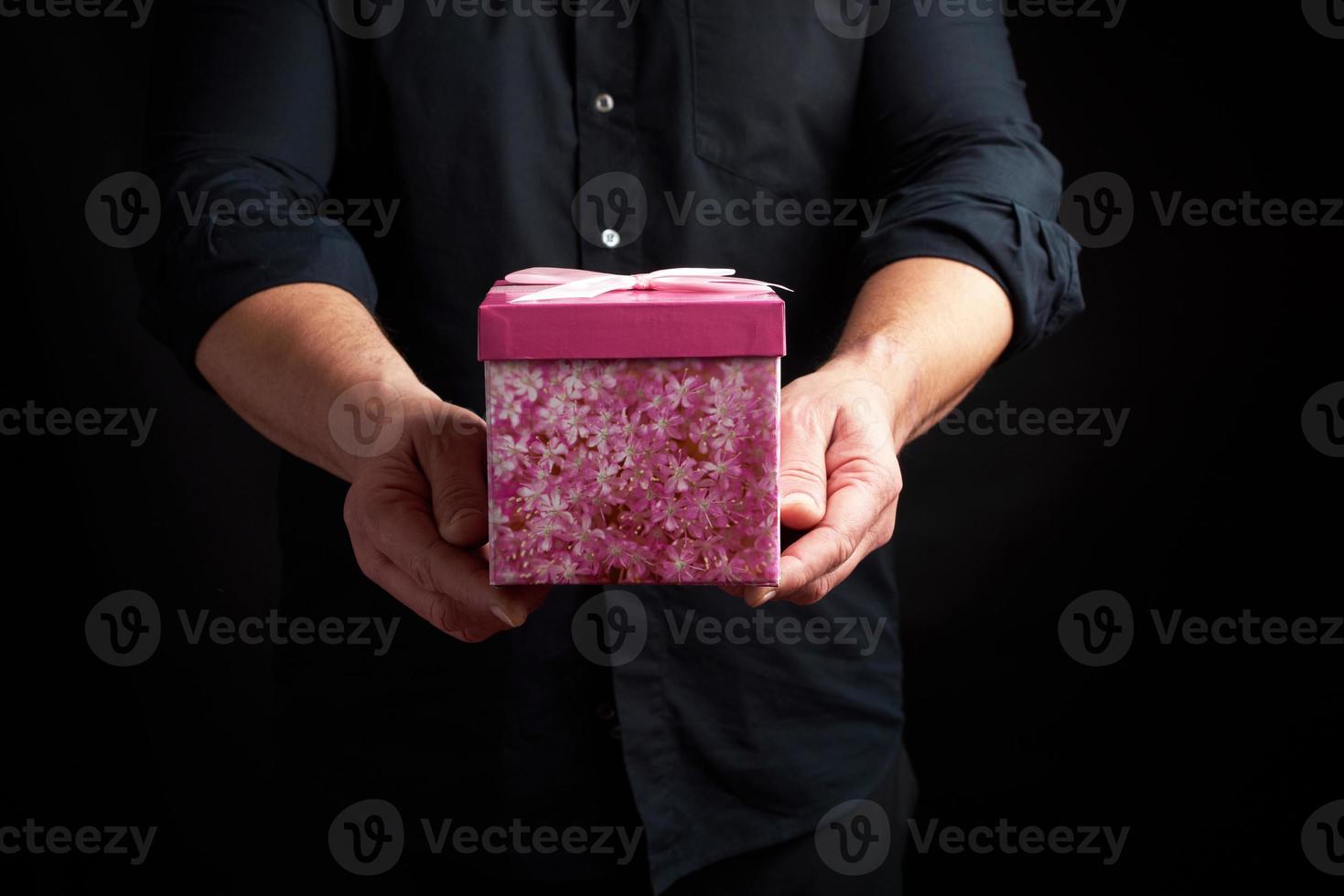 adult man in a black shirt holds a pink square box with a bow photo