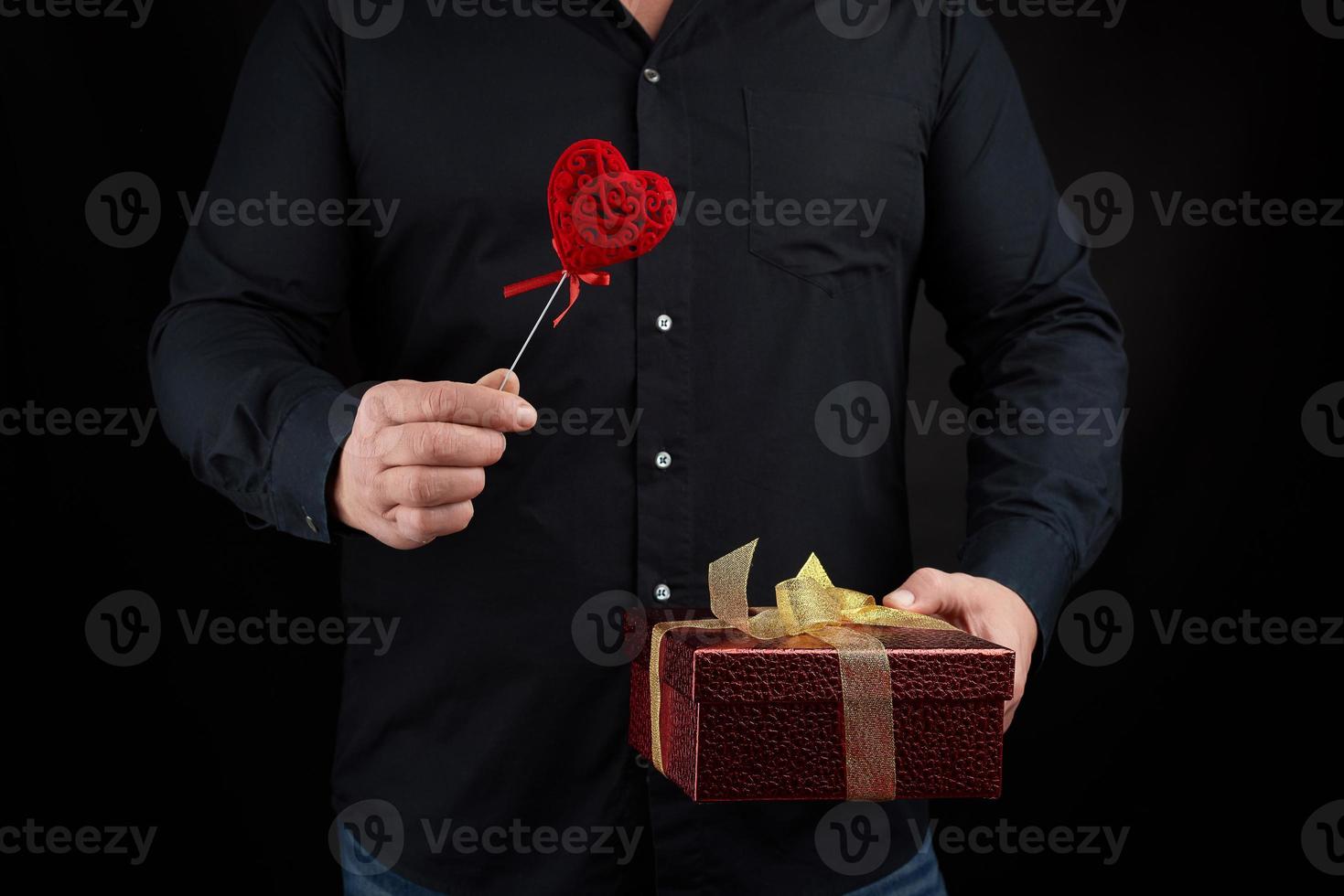 an adult man in a black shirt holds in his hand a red cardboard box tied with a golden bow photo