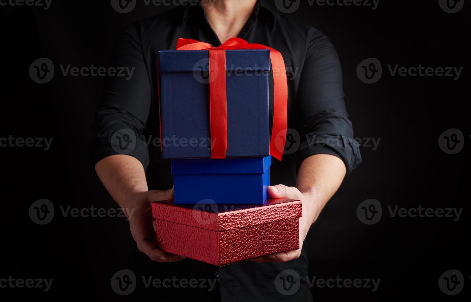 adult man in a black shirt holds in his hands a stack of paper-wrapped gifts on a black background photo