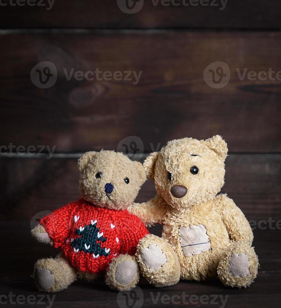 two brown soft teddy bears are sitting on a wooden surface photo