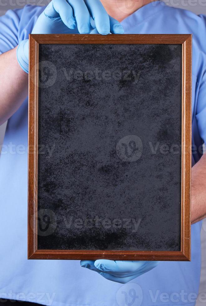 doctor in blue uniform and latex sterile gloves holding a blank black frame photo