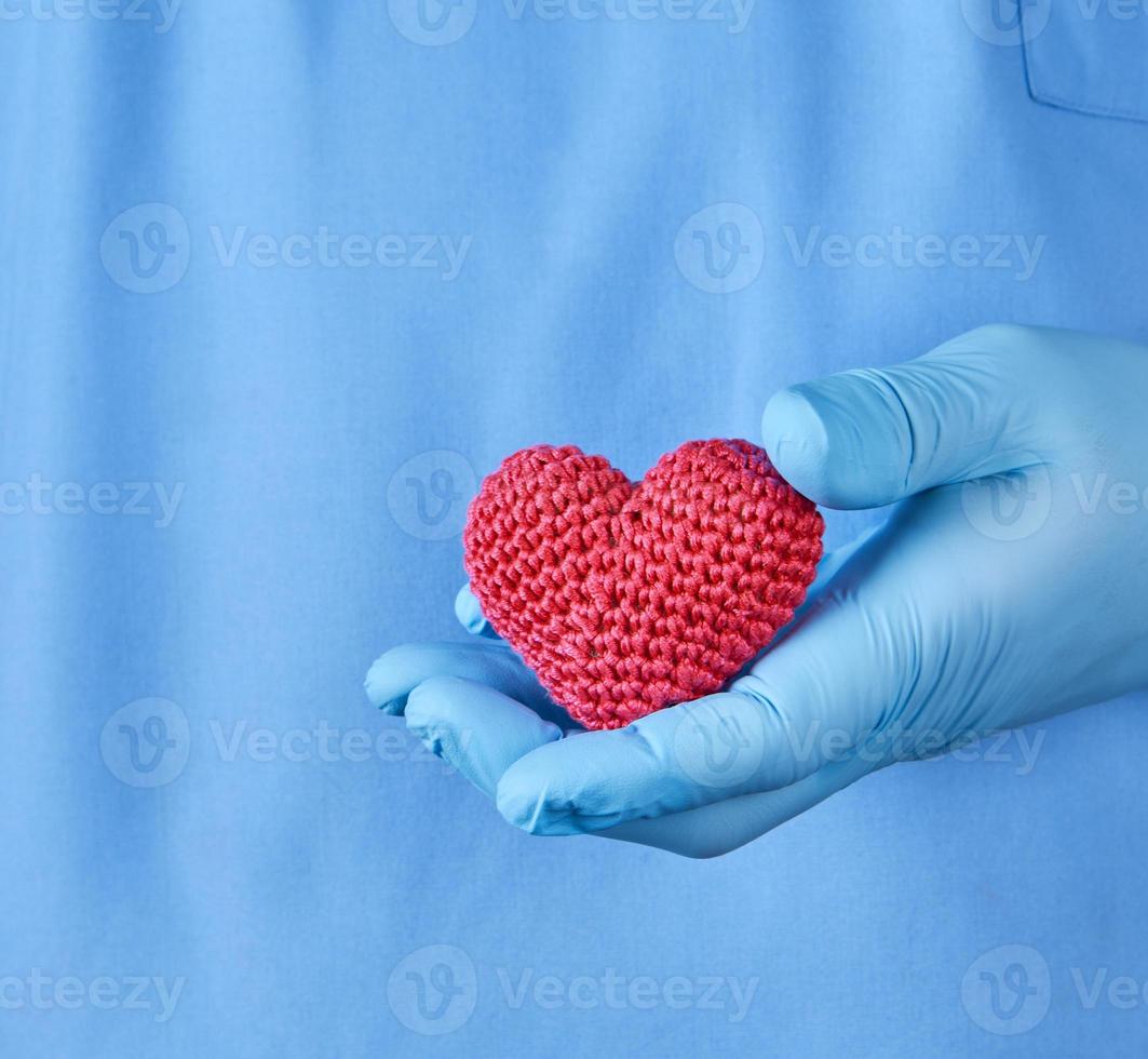 doctor with blue latex gloves holding a red heart photo