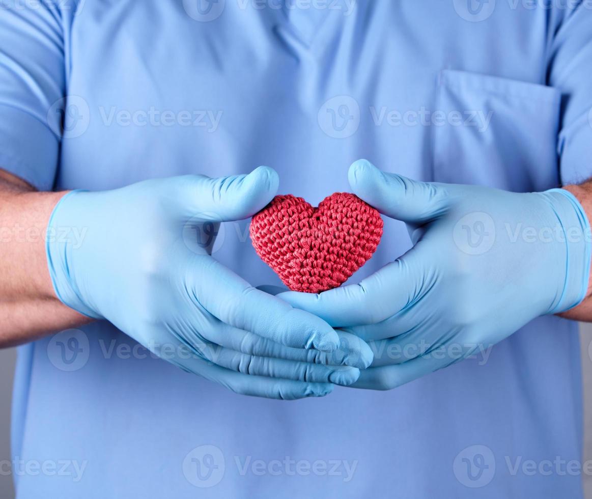 doctor with blue latex gloves holding a red heart photo