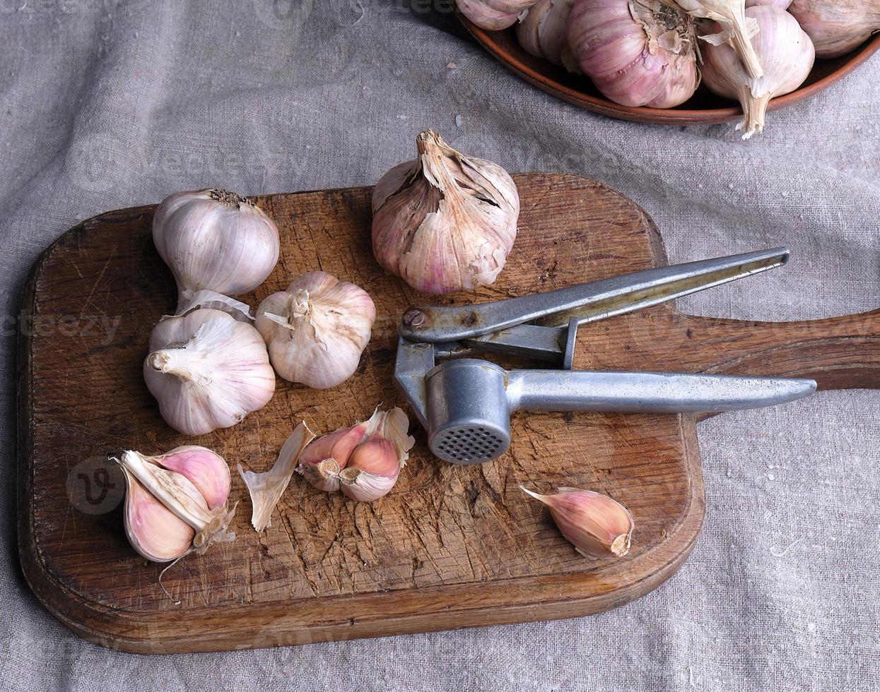 raw unpeeled garlic on a very old vintage cutting board and an iron extruder photo