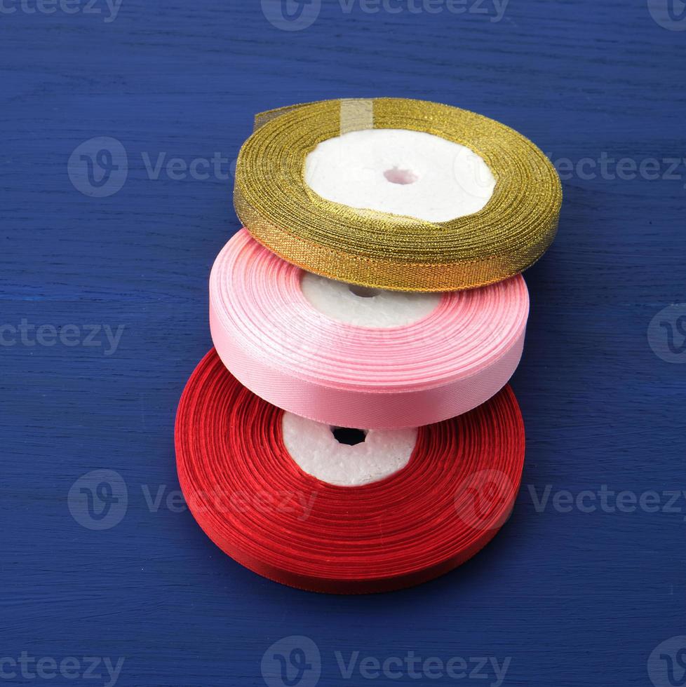 twisted red, pink, golden silk ribbons on a blue background, element for the designer, top view photo